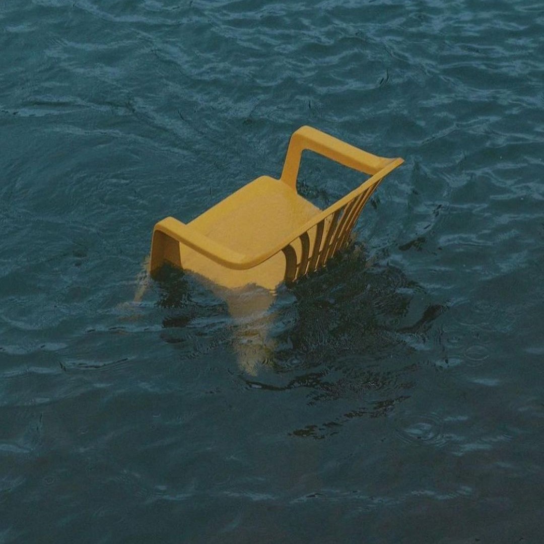 A yellow plastic chair half-sunk in dark green water.